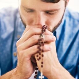 Putting his faith first. Cropped shot of a young man holding his rosary while praying.